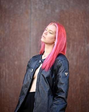 Portrait of Soë Blue with pink hair wearing a black leather jacket against a brown background