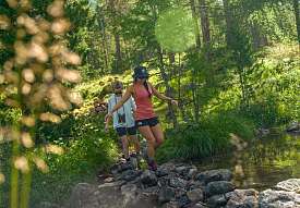 Due donne attraversano un ruscello durante un’escursione nel bosco vicino a Pontresina nelle Alpi dell’Engadina