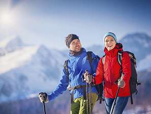 Zwei fröhliche Winterwanderer mit Stöcken und Rucksäcken vor verschneitem Bergpanorama in Pontresina.
