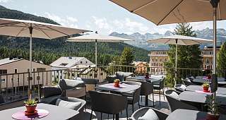 Terrazza soleggiata con aree lounge, ombrelloni e vista sulle montagne